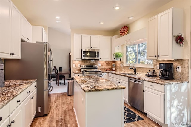 kitchen with light stone countertops, light wood-type flooring, a kitchen island, stainless steel appliances, and white cabinets