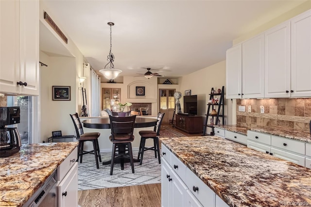 kitchen with light stone countertops, hanging light fixtures, ceiling fan, light hardwood / wood-style floors, and white cabinets