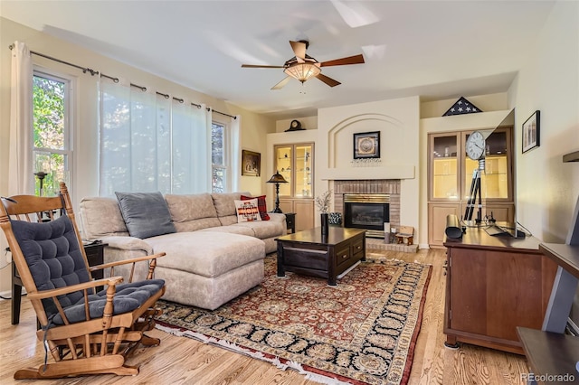 living room featuring ceiling fan, light wood-type flooring, and a brick fireplace