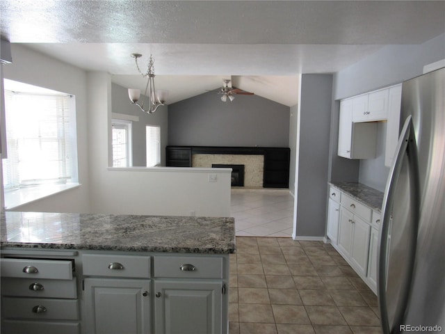 kitchen featuring white cabinetry, lofted ceiling, stainless steel refrigerator, dark stone countertops, and pendant lighting