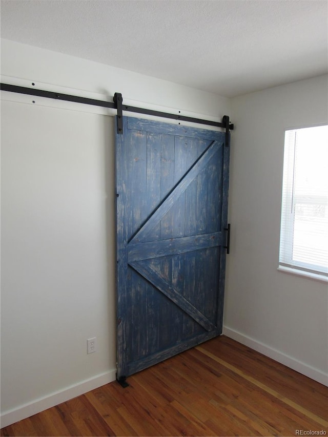 unfurnished room with a textured ceiling, dark wood-type flooring, and a barn door