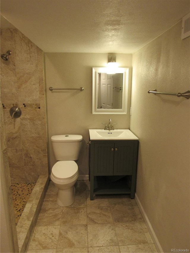 bathroom featuring a textured ceiling, toilet, vanity, and tiled shower