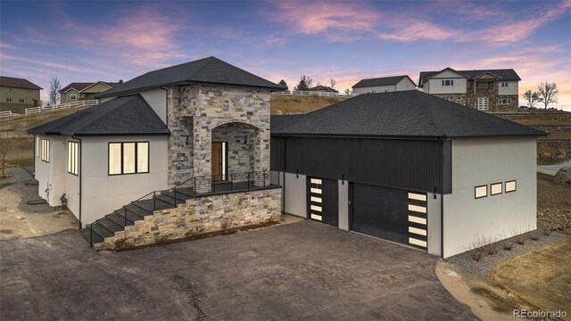 view of front of house with a garage, stone siding, aphalt driveway, and roof with shingles