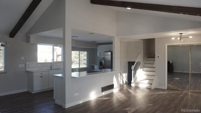 kitchen featuring decorative backsplash, stainless steel refrigerator with ice dispenser, white cabinets, sink, and beam ceiling