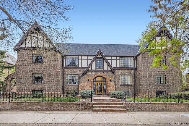 english style home with a fenced front yard and brick siding