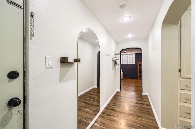 hall with arched walkways, baseboards, and wood finished floors