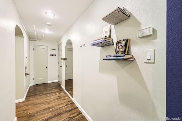 corridor with arched walkways, baseboards, and wood finished floors