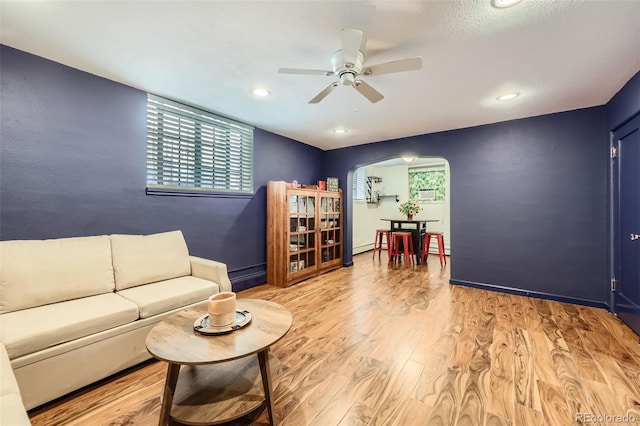 living room with arched walkways, light wood-style flooring, a ceiling fan, recessed lighting, and a baseboard heating unit