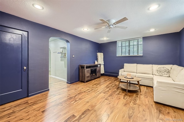 living area with a ceiling fan, a textured ceiling, arched walkways, light wood-type flooring, and baseboards
