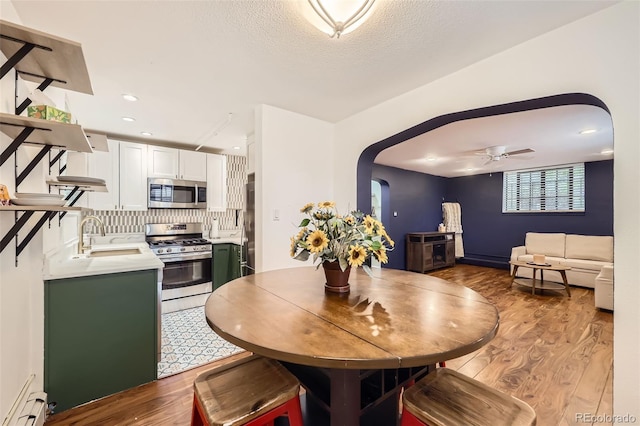 dining area featuring light wood-style floors, arched walkways, a ceiling fan, and a baseboard heating unit