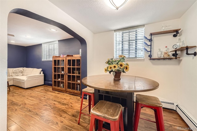 dining room featuring arched walkways, baseboard heating, a textured ceiling, and wood finished floors
