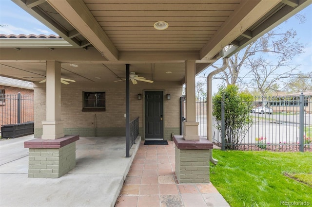 view of exterior entry featuring fence, ceiling fan, and brick siding