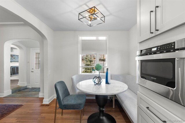 dining room featuring arched walkways, wood finished floors, and baseboards