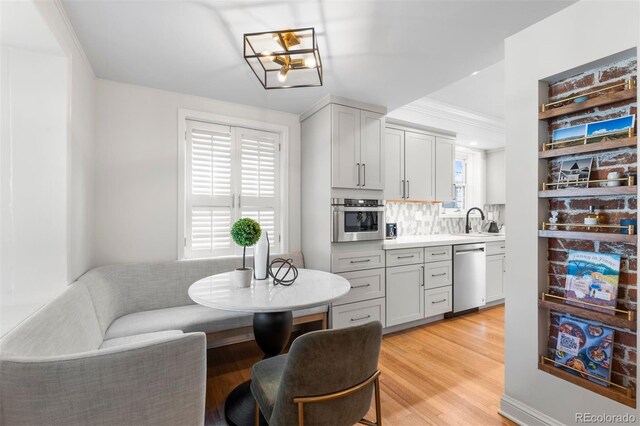 kitchen featuring stainless steel appliances, a sink, decorative backsplash, light countertops, and light wood-style flooring