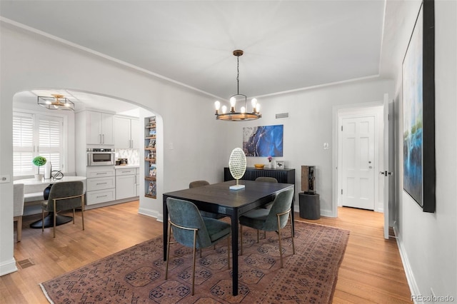 dining space with arched walkways, a chandelier, light wood-style floors, and baseboards