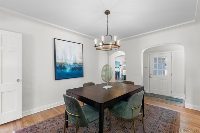 dining space featuring arched walkways, a chandelier, wood finished floors, baseboards, and ornamental molding