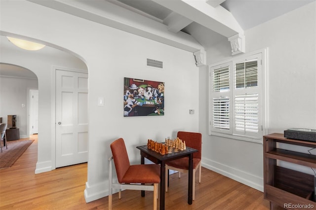 dining space featuring arched walkways, light wood finished floors, baseboards, and vaulted ceiling