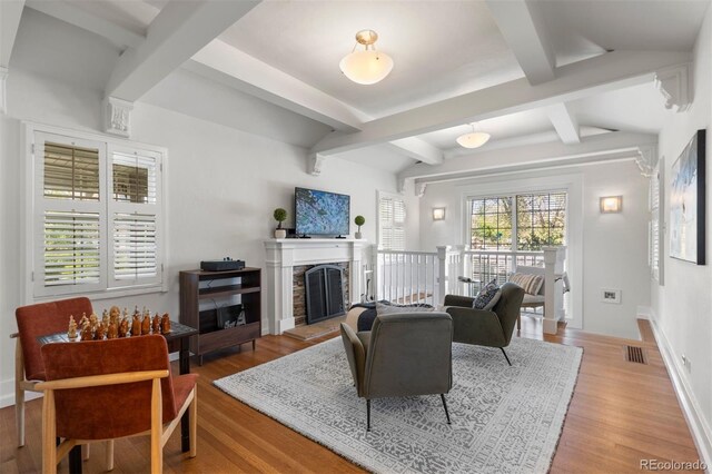 living room featuring wood finished floors, beam ceiling, a fireplace with raised hearth, and baseboards