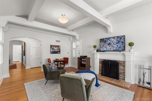 living room featuring arched walkways, light wood-style flooring, beam ceiling, a fireplace, and baseboards