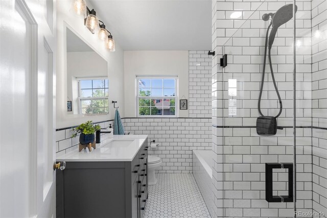 full bath with tile walls, a tile shower, vanity, tile patterned floors, and toilet