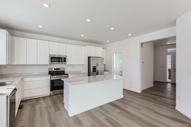 kitchen featuring white cabinetry, stainless steel appliances, a kitchen island, and light wood-type flooring