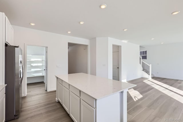 kitchen with stainless steel fridge, light hardwood / wood-style flooring, a center island, light stone counters, and white cabinets