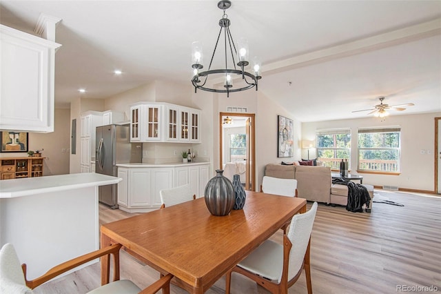 dining room with ceiling fan with notable chandelier, lofted ceiling, and light hardwood / wood-style flooring