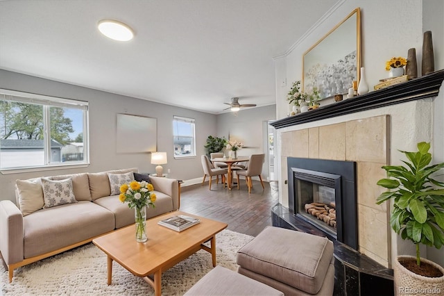 living room with a tiled fireplace, dark wood-type flooring, a healthy amount of sunlight, and ceiling fan