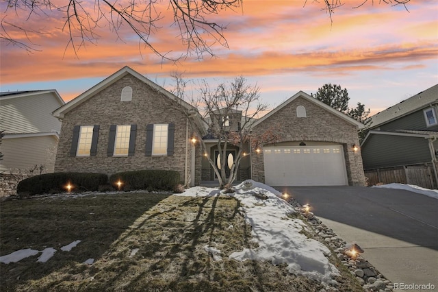 view of front of property featuring a yard, stone siding, an attached garage, and driveway