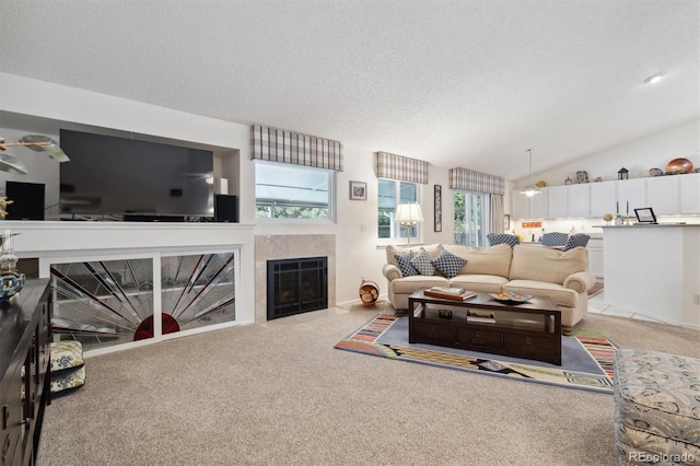 carpeted living room with a tiled fireplace, a wealth of natural light, lofted ceiling, and a textured ceiling