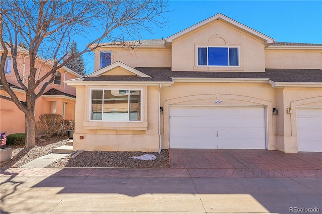 view of front of house featuring a shingled roof, decorative driveway, an attached garage, and stucco siding