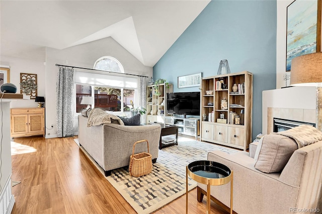 living area featuring high vaulted ceiling, a tile fireplace, and wood finished floors