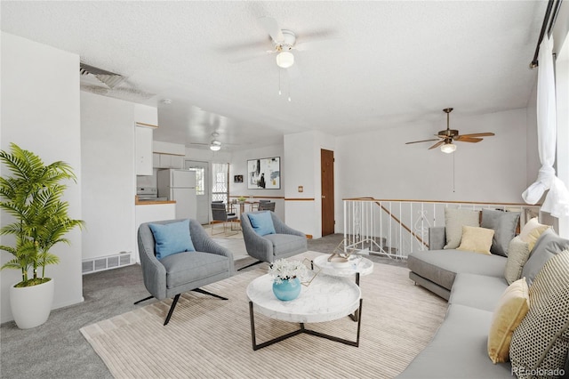 living room with visible vents, a textured ceiling, ceiling fan, and light colored carpet