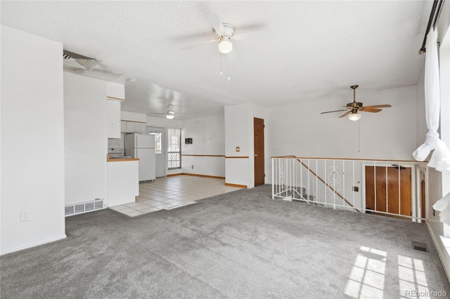 unfurnished living room with light tile patterned flooring, ceiling fan, visible vents, and light carpet