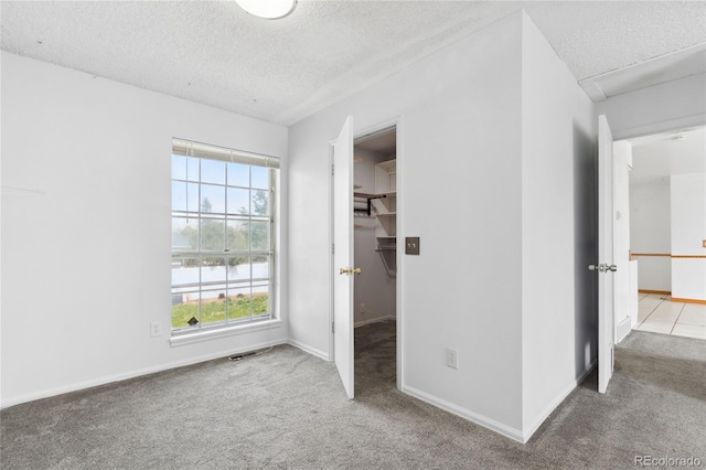 unfurnished bedroom featuring carpet floors, a textured ceiling, baseboards, a spacious closet, and visible vents