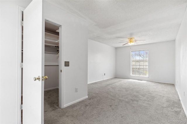 unfurnished bedroom featuring carpet flooring, ceiling fan, a textured ceiling, baseboards, and a spacious closet