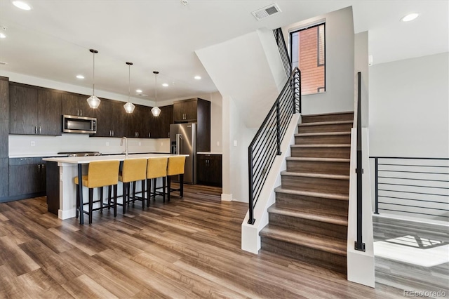 kitchen featuring visible vents, a breakfast bar area, wood finished floors, stainless steel appliances, and dark brown cabinets