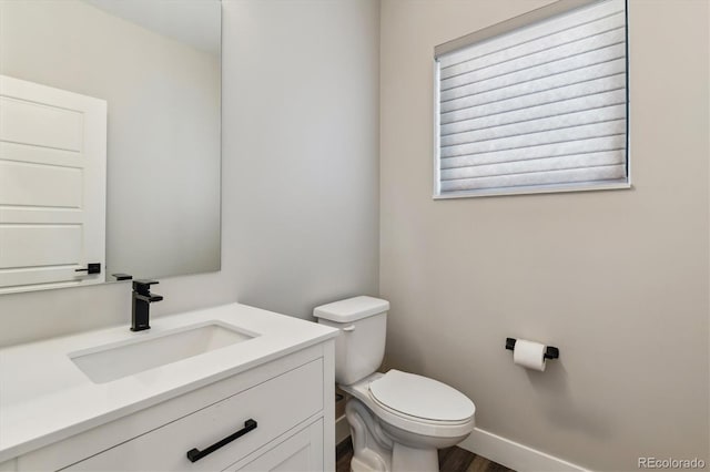 half bathroom with baseboards, vanity, and toilet