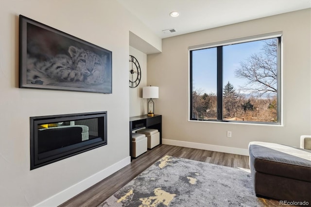 living area featuring baseboards, visible vents, a glass covered fireplace, wood finished floors, and recessed lighting