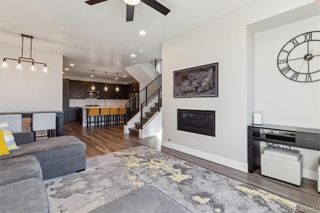 living area with baseboards, dark wood finished floors, a glass covered fireplace, stairway, and recessed lighting