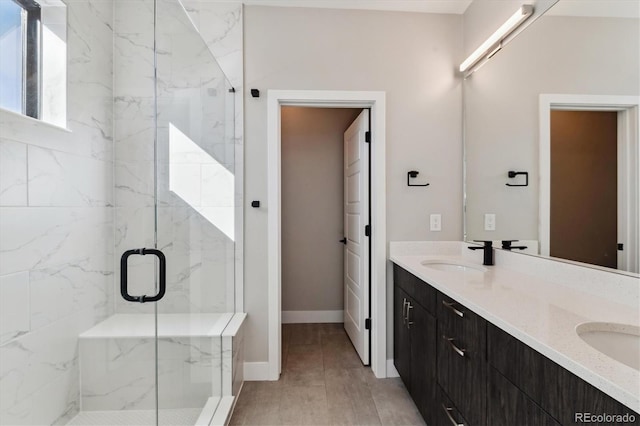 full bathroom with double vanity, a marble finish shower, baseboards, and a sink