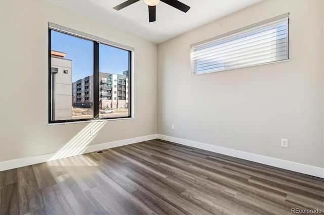 spare room with dark wood-style floors, visible vents, ceiling fan, and baseboards