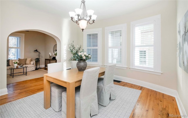 dining space with a chandelier, arched walkways, baseboards, and wood finished floors