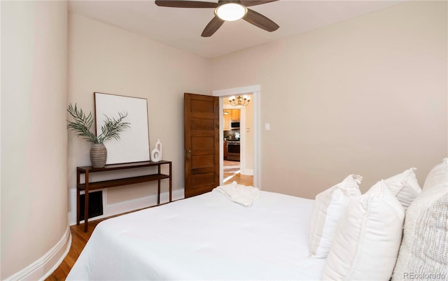 bedroom with ceiling fan with notable chandelier, wood finished floors, and baseboards