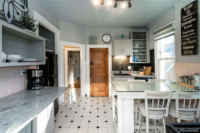 kitchen featuring white cabinets, decorative backsplash, a breakfast bar, open shelves, and a sink