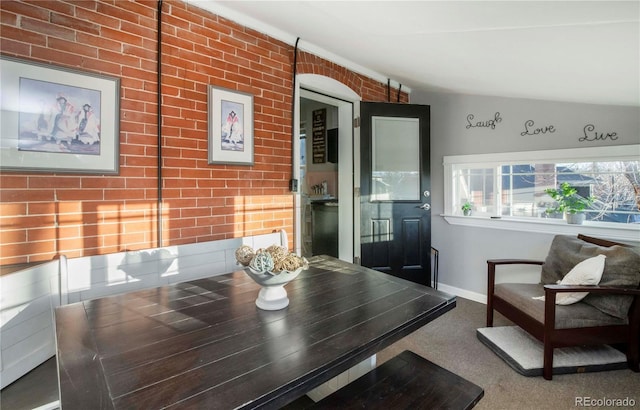 dining room featuring brick wall, baseboards, and vaulted ceiling