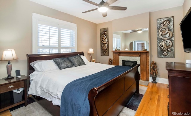 bedroom with light wood-style floors, ceiling fan, a fireplace, and baseboards