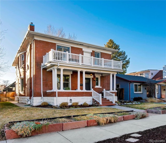 view of front of home with brick siding, a chimney, covered porch, a balcony, and a front lawn