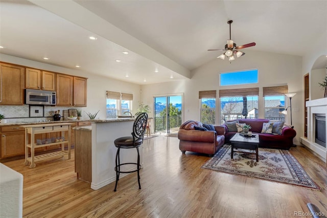 kitchen with light wood finished floors, open floor plan, a glass covered fireplace, stainless steel microwave, and tasteful backsplash