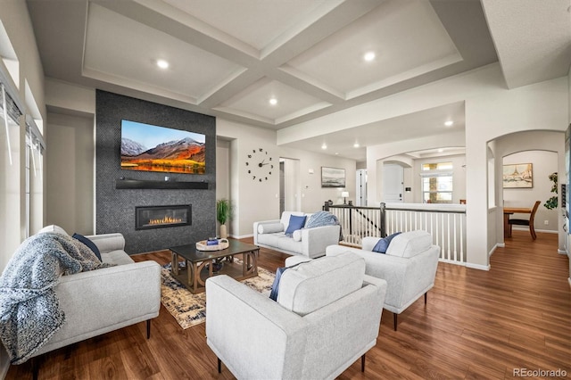 living area with arched walkways, a large fireplace, wood finished floors, coffered ceiling, and baseboards